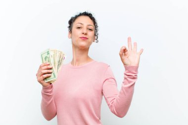 Beyaz duvarda banknotları olan genç ve güzel bir kadın.