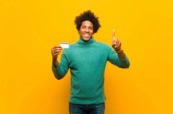 Joven afroamericano hombre con una tarjeta de crédito contra bac naranja — Foto de Stock