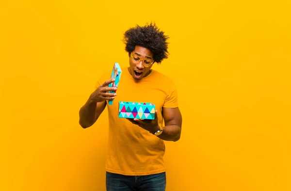Joven afroamericano hombre con una caja de regalo contra fondo naranja — Foto de Stock