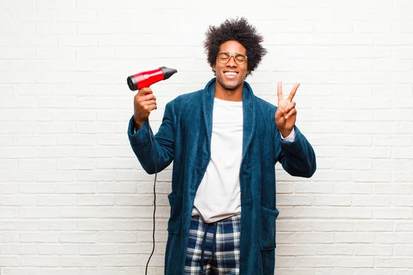 Ung svart man bär pyjamas med en hårtork mot tegel — Stockfoto