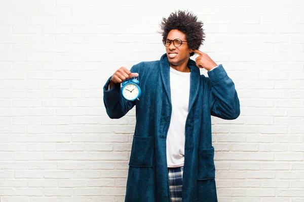 young black man wearing pajamas with an alarm clock
