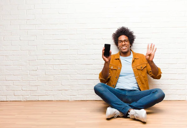 Mladý černošky muž s chytrým telefonem sedí na podlaze — Stock fotografie