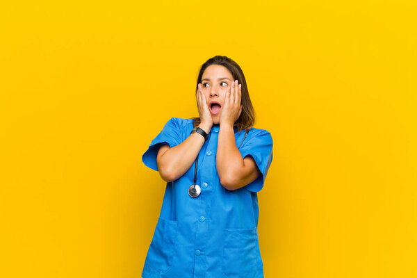 feeling happy, excited and surprised, looking to the side with both hands on face isolated against yellow wall