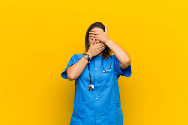 covering face with both hands saying no to the camera! refusing pictures or forbidding photos isolated against yellow wall