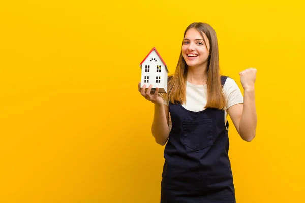 Junge Hübsche Frau Mit Hausmodell Vor Orangefarbenem Hintergrund — Stockfoto