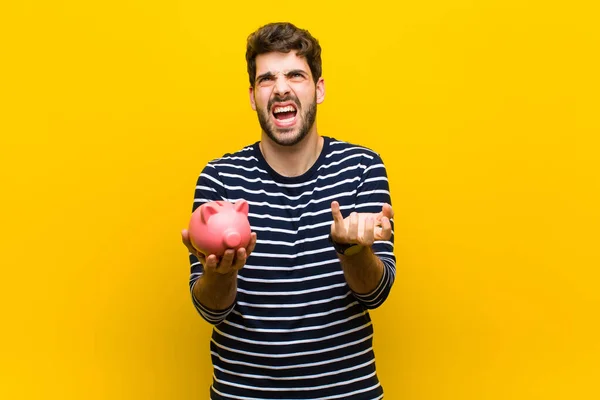 Ung stilig man som håller en spargris mot orange backgroun — Stockfoto