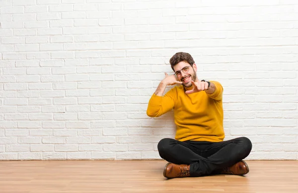 レンガの壁のテクスチャに対して家の床に座っている若いハンサムな男 — ストック写真