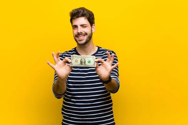 Молодой красивый мужчина с долларовыми банкнотами против оранжевого бэкгру — стоковое фото