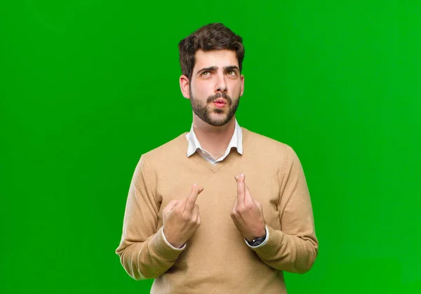 young businessman crossing fingers anxiously and hoping for good luck with a worried look against green background