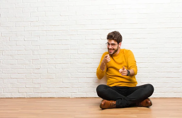 レンガの壁のテクスチャに対して家の床に座っている若いハンサムな男 — ストック写真