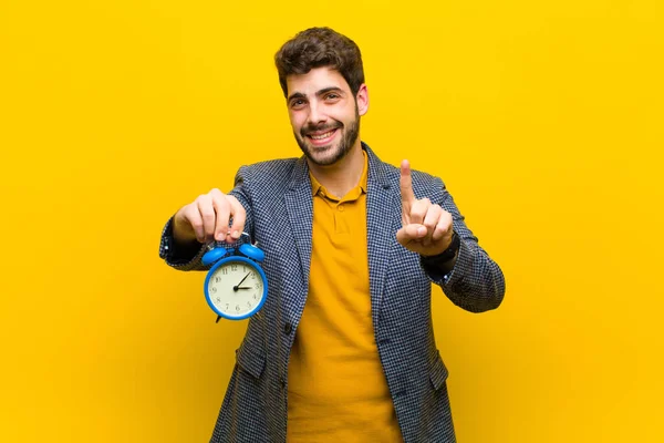 Joven hombre guapo con un reloj despertador sobre fondo naranja — Foto de Stock