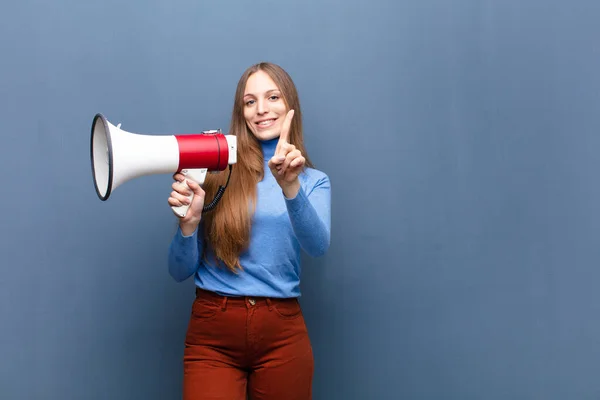 young pretty woman with a megaphone against blue wall with a copy space