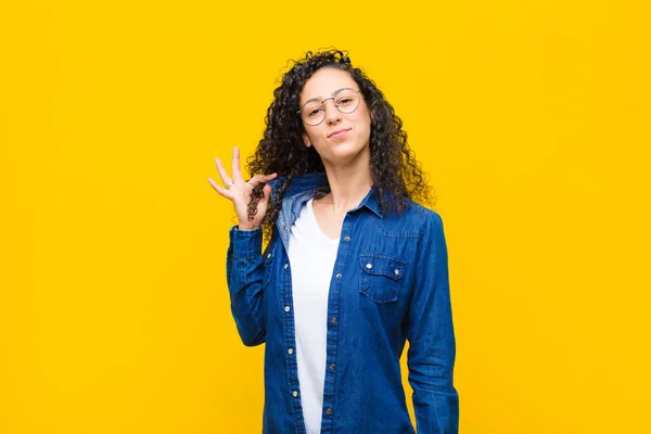 young pretty woman looking arrogant, successful, positive and proud, pointing to self against orange wall