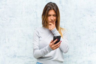 Akıllı telefonlu güzel bir kadın grunge duvarına karşı.