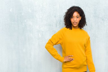 Genç, güzel, siyah bir kadın mutlu bir şekilde gülümsüyor. Elini kalçasında ve kendinden emin, olumlu, gururlu ve arkadaş canlısı bir tavırla.