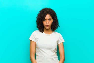 Genç siyahi kadın üzgün, üzgün ya da kızgın hissediyor ve olumsuz bir tavırla, mavi duvara karşı anlaşmazlıkla bakıyor.
