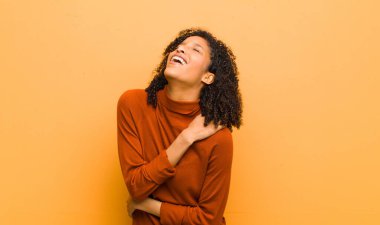 Genç, güzel, siyah bir kadın endişeli, hasta, hasta ve mutsuz hissediyor. Ağrılı bir mide ağrısı ya da turuncu duvarda grip geçiriyor.