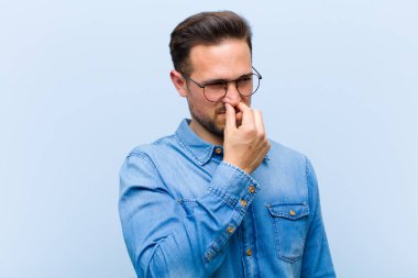 Genç yakışıklı adam iğreniyor, kötü ve nahoş bir koku duymamak için burnunu tutuyor.