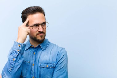 Yoğunlaşmış bakışları olan genç yakışıklı bir adam şüpheli bir ifadeyle yukarı ve yana bakıyor.