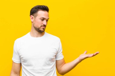 Genç yakışıklı adam mutlu ve gülümsüyor. Turuncu duvara karşı elinde tuttuğu bir nesneye ya da konsepte bakıyor.