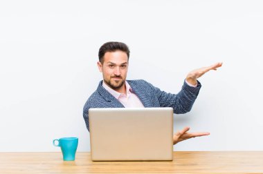 Genç yakışıklı iş adamı, iki eli de kenarda duran bir objeyi tutuyor, fotokopi alanında, bir nesneyi gösteriyor, sunuyor ya da reklamını yapıyor.