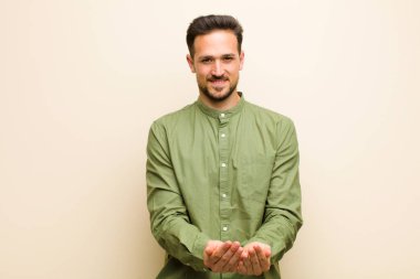 Genç yakışıklı adam mutlu bir şekilde gülümsüyor arkadaş canlısı, kendinden emin, olumlu bakışlı, bir nesne ya da konsept sunuyor ve gösteriyor.