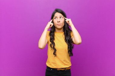 Genç ve güzel Latin kadın konsantre olmuş ve bir fikir üzerinde kafa yoruyor, mor duvara karşı bir meydan okuma veya soruna bir çözüm hayal ediyor.