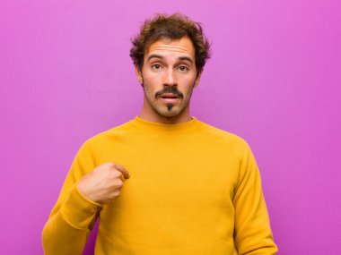 Kafası karışmış, kafası karışmış ve kendine güveni olmayan genç yakışıklı bir adam kendini gösterip kim olduğumu soruyor, ben mi? mor duvara yaslan