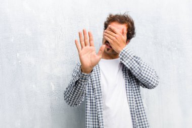 Genç ve yakışıklı bir adam elleriyle yüzünü kapatıyor ve kamerayı durdurmak için diğer elini öne koyuyor. Duvara yaslanmış fotoğraf ve resimleri reddediyor.