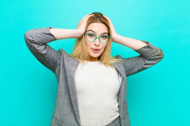 Genç, güzel sarışın kadın heyecanlı ve şaşırmış görünüyor, ağzı açık, iki eli başının üstünde, düz duvara karşı şanslı bir kazanan gibi hissediyor.