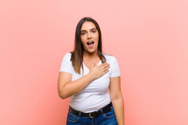 Genç ve güzel İspanyol kadın şok olmuş ve şaşırmış hissediyor, gülümsüyor, el ele tutuşuyor, o kişi olmaktan mutlu ya da pembe duvara karşı minnettarlık gösteriyor.