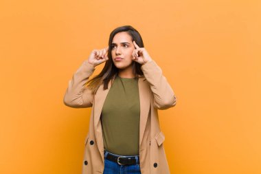 Genç, güzel bir kadın, kafası karışmış ya da şüpheye düşmüş, bir fikre odaklanmış, çok düşünüyor, turuncu duvara karşı boşluğu kopyalamak istiyor.