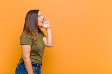 Genç ve güzel bir kadın profili, mutlu ve heyecanlı görünüyor, bağırıyor ve turuncu duvara karşı izole edilmiş bir şekilde kopyalama alanı istiyor.