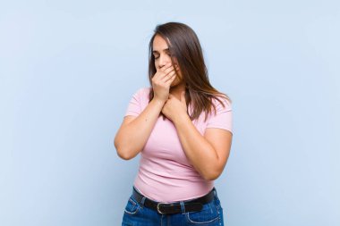 Gırtlağı ağrıyan ve grip belirtileri gösteren, ağzı mavi arka planda öksüren genç ve güzel bir kadın.