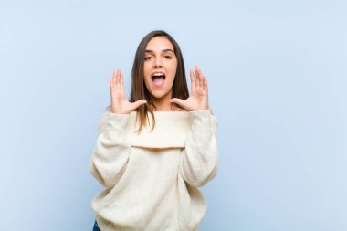 Genç ve güzel bir kadın mavi arka planda beklenmedik bir sürprizden dolayı şaşkın ve heyecanlı, güler yüzlü, şaşkın ve mutlu hissediyor.