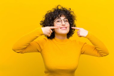 Genç, güzel afro kadın, kendine güvenerek gülümsüyor. Geniş bir gülümseme, pozitif, rahat, tatmin olmuş bir tavır sergiliyor.