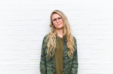 Genç sarışın kadın kafası karışık ve şüpheli hissediyor, merak ediyor ya da tuğla duvar arkasında bir karar vermeye çalışıyor.