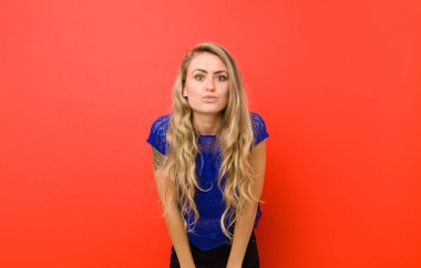 Genç sarışın kadın dudaklarını birbirine bastırıyor, tatlı, eğlenceli, mutlu, sevimli bir yüz ifadesiyle, kırmızı duvara öpücük yolluyor.