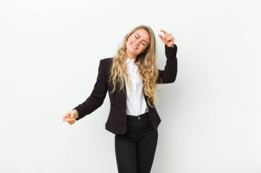 Genç sarışın kadın gülümsüyor, kaygısız hissediyor, rahat ve mutlu, dans ediyor ve müzik dinliyor, beyaz duvarın karşısındaki bir partide eğleniyor.