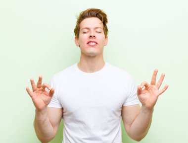 Genç kızıl saçlı yakışıklı adam konsantre olmuş ve meditasyon yapıyor, tatmin olmuş ve rahatlamış hissediyor, düşünüyor ya da bir seçim yapıyor.
