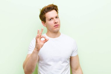 Genç kızıl saçlı yakışıklı adam mutlu, rahat ve tatmin olmuş hissediyor. Onayını iyi bir hareketle gösteriyor. Gülümsüyor.