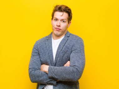 Genç kızıl saçlı adam omuz silkiyor, kafası karışık ve emin değil, kolları bağlı ve şaşkın görünüyor turuncu arka planda