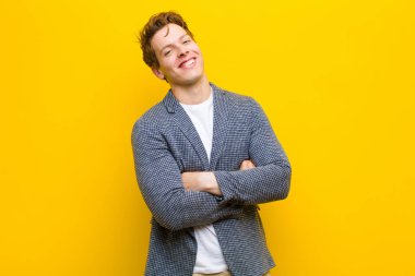 Genç kızıl saçlı adam kollarını kavuşturup mutlu bir şekilde gülüyor. Turuncu arka planda rahat, pozitif ve tatmin olmuş bir duruşu var.