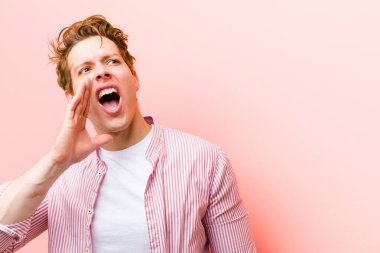 Genç kızıl saçlı adam öfkeyle bağırıyor kenardaki boşluğu kopyalamak için, eli ağzının yanında pembe duvara yaslanmış.
