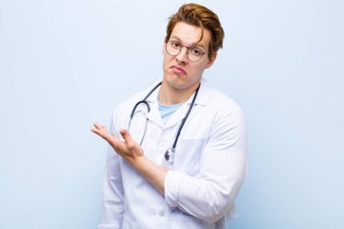 Genç kızıl kafalı doktor, kafası karışık ve bilgisiz hissediyor, şüpheli bir açıklamayı merak ediyor ya da mavi duvara karşı düşüncelerini merak ediyor.