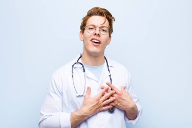 Genç kızıl saçlı doktor romantik, mutlu ve aşık, neşeyle gülümseyen ve mavi duvara yakın el ele tutuşan