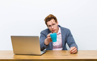 Genç kızıl saçlı işadamı masasında sıcak bir kahve bardağıyla çalışıyor.