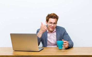 Genç kızıl saçlı işadamı masasında sıcak bir kahve bardağıyla çalışıyor.