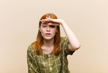 Genç kızıl saçlı güzel kadın şaşkınlık ve şaşkınlık içinde bakıyor, el üstünde, uzaklara bakıyor, izliyor ya da arıyor.