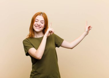 Genç kızıl saçlı güzel kadın mutlu bir şekilde gülümsüyor ve her iki elini de fotokopi uzayında nesne göstererek yukarı ve yana doğru gösteriyor.